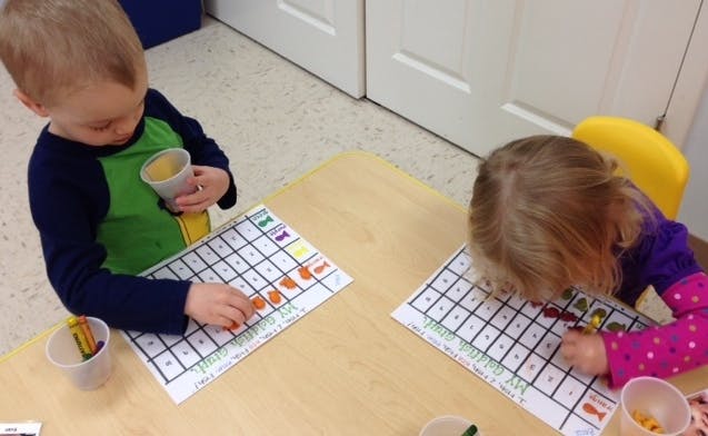 Two children at a table with grid papers and small objects