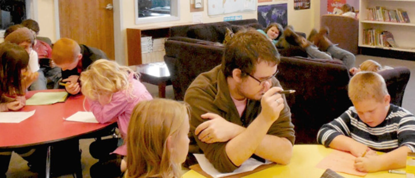 People and children sitting at tables, some writing