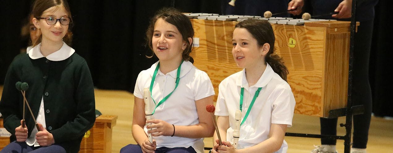 Three children with musical instruments, including recorders and mallets