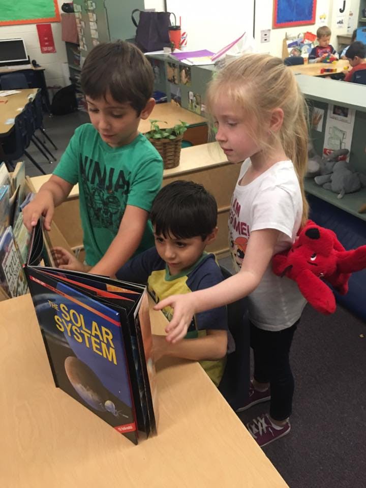 Three children looking at a book titled "Solar System"