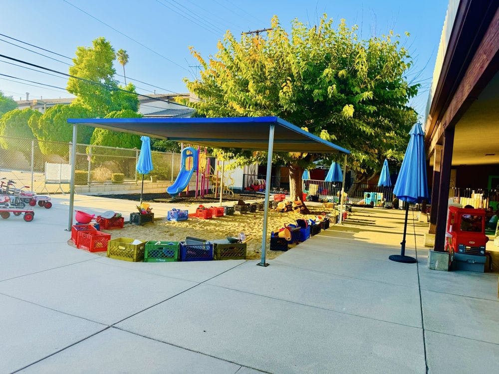 Outdoor playground with a blue slide, shade structure, and umbrellas