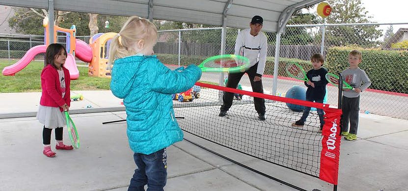 Children and an adult playing with rackets and a net