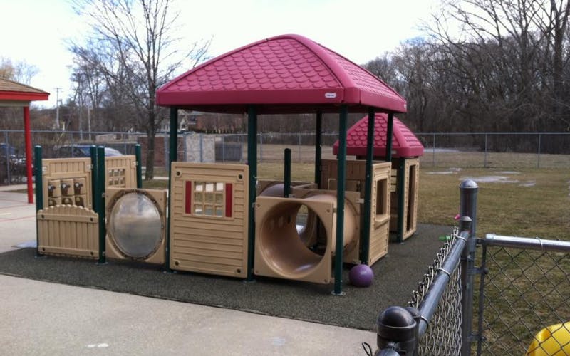 Empty children's playground with a red roof, tan panels, and tunnel