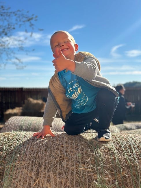 Child kneeling on hay bale giving a thumbs up