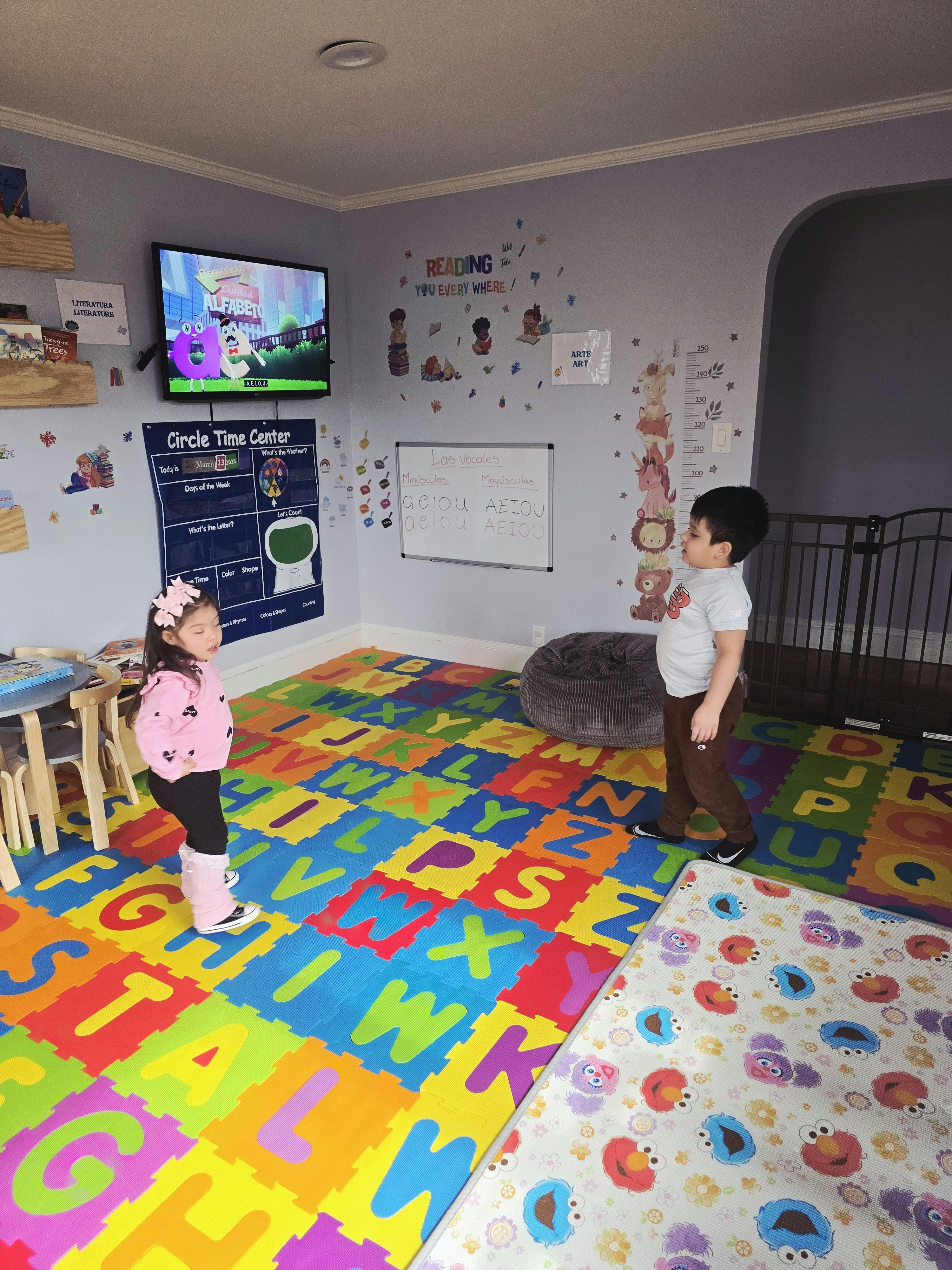 A child in a pink shirt standing on alphabet matting, another child nearby