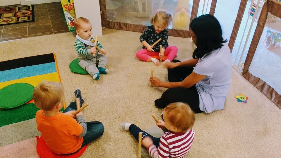 Adult and children sitting on floor in a circle holding drumsticks