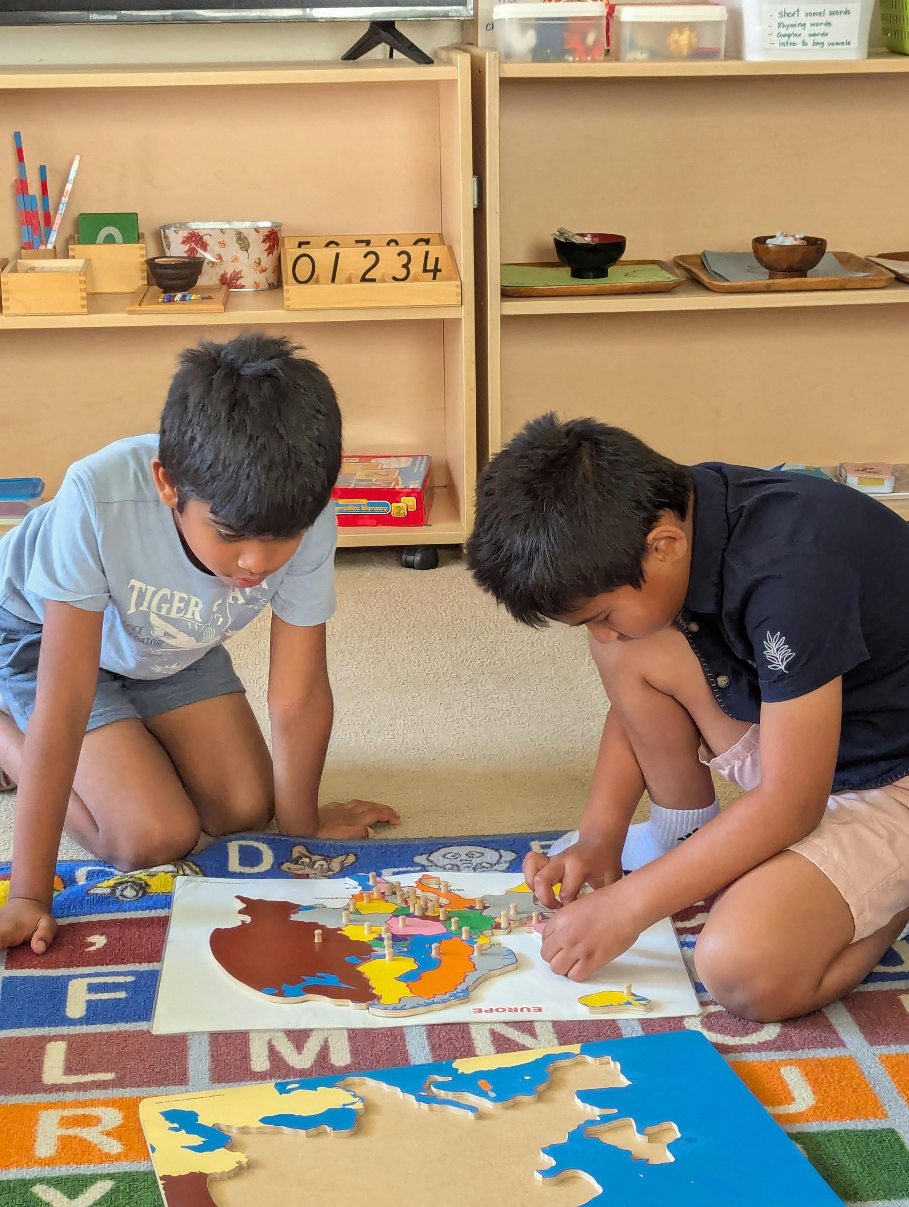 Two children kneeling on a rug, assembling a world map puzzle
