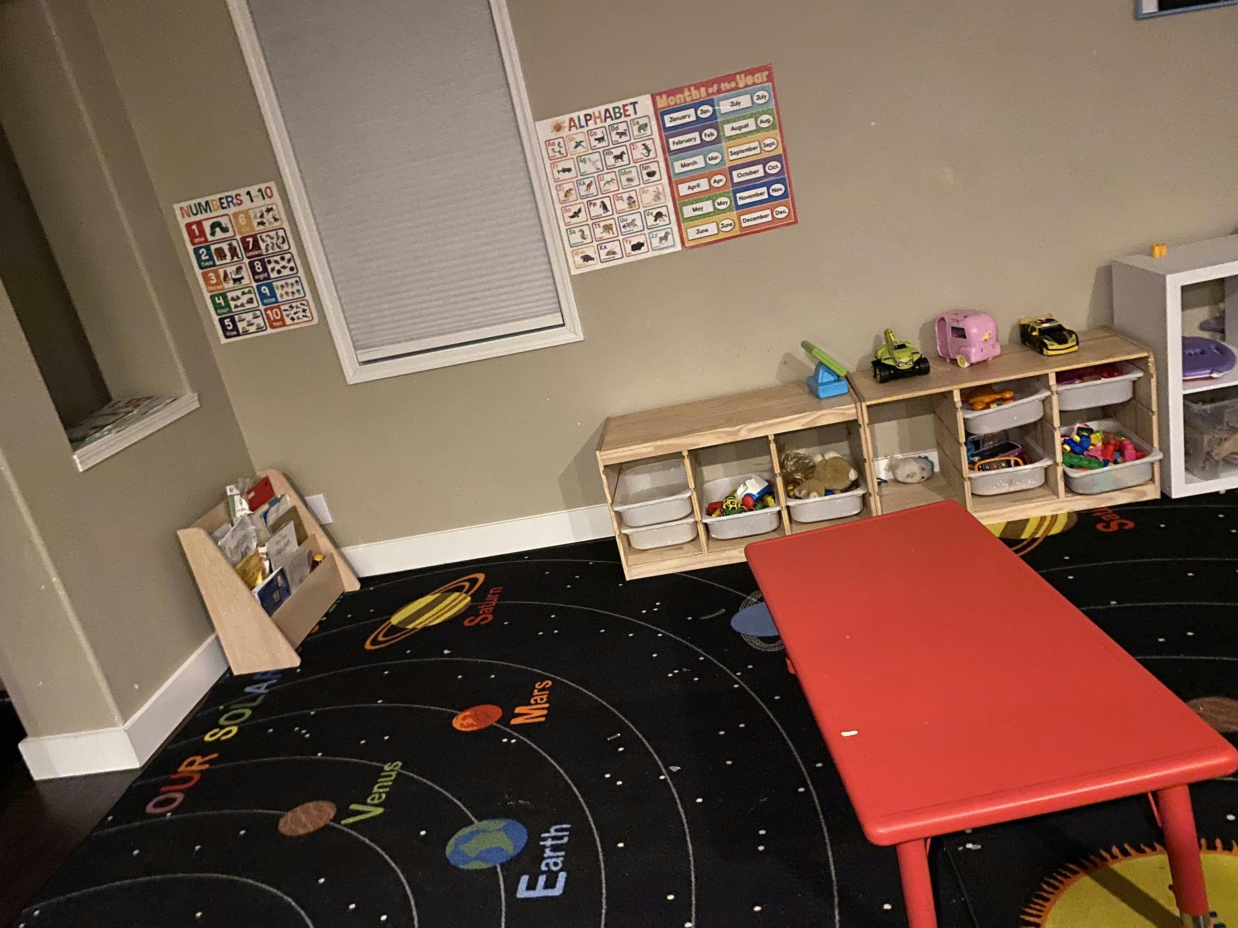 Playroom with a solar system rug, red table, and toy storage