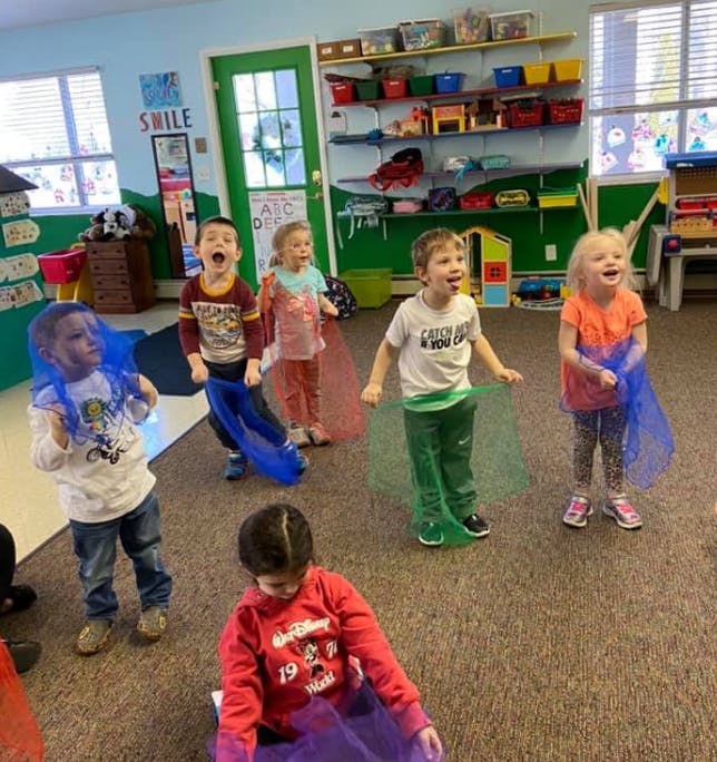 Children playing with colorful sheer fabric in a classroom
