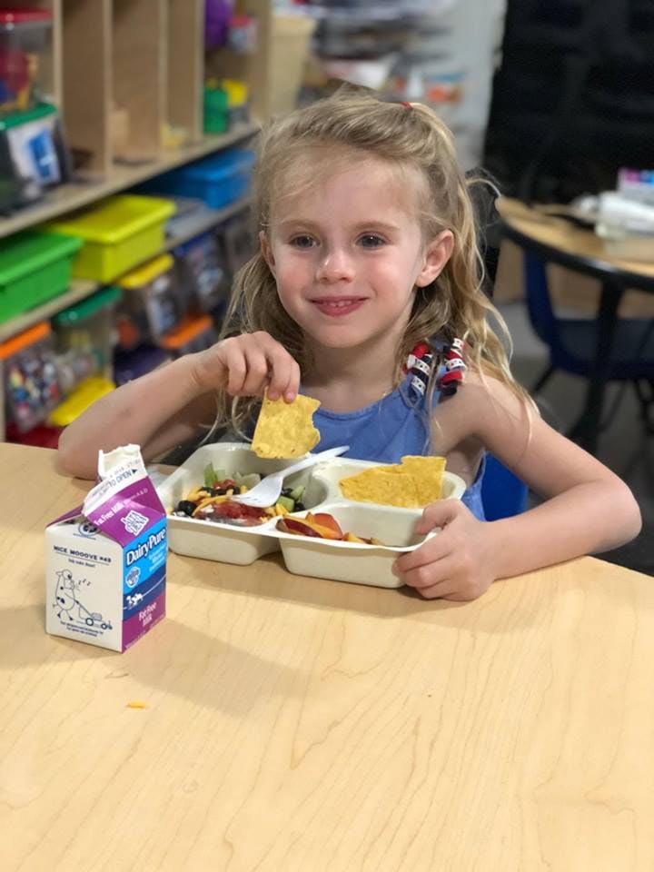 Child eating from a school lunch tray with a milk carton on the table
