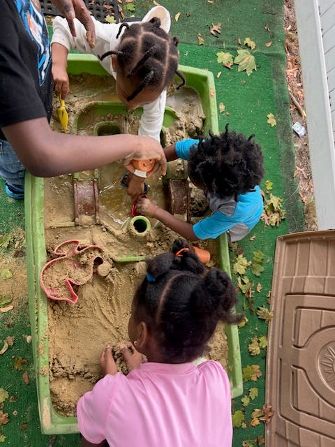 Person and two children playing in a sand table
