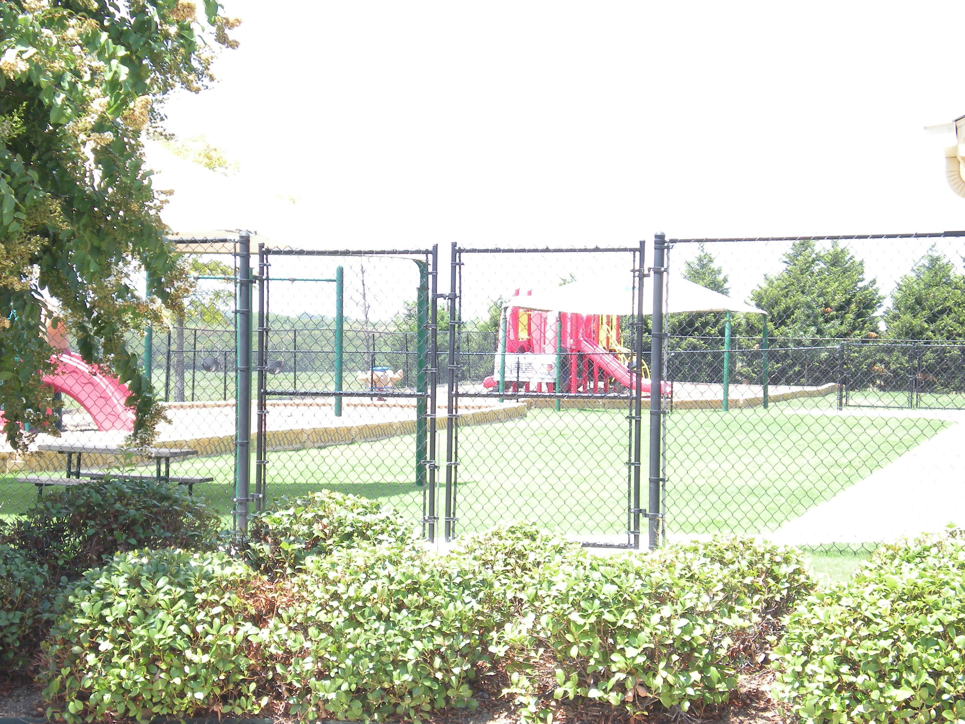Playground with chain link fence and bushes in the background a red slide