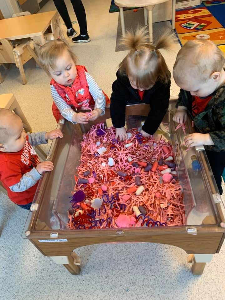 Three children playing with shredded paper and small objects in a sensory table