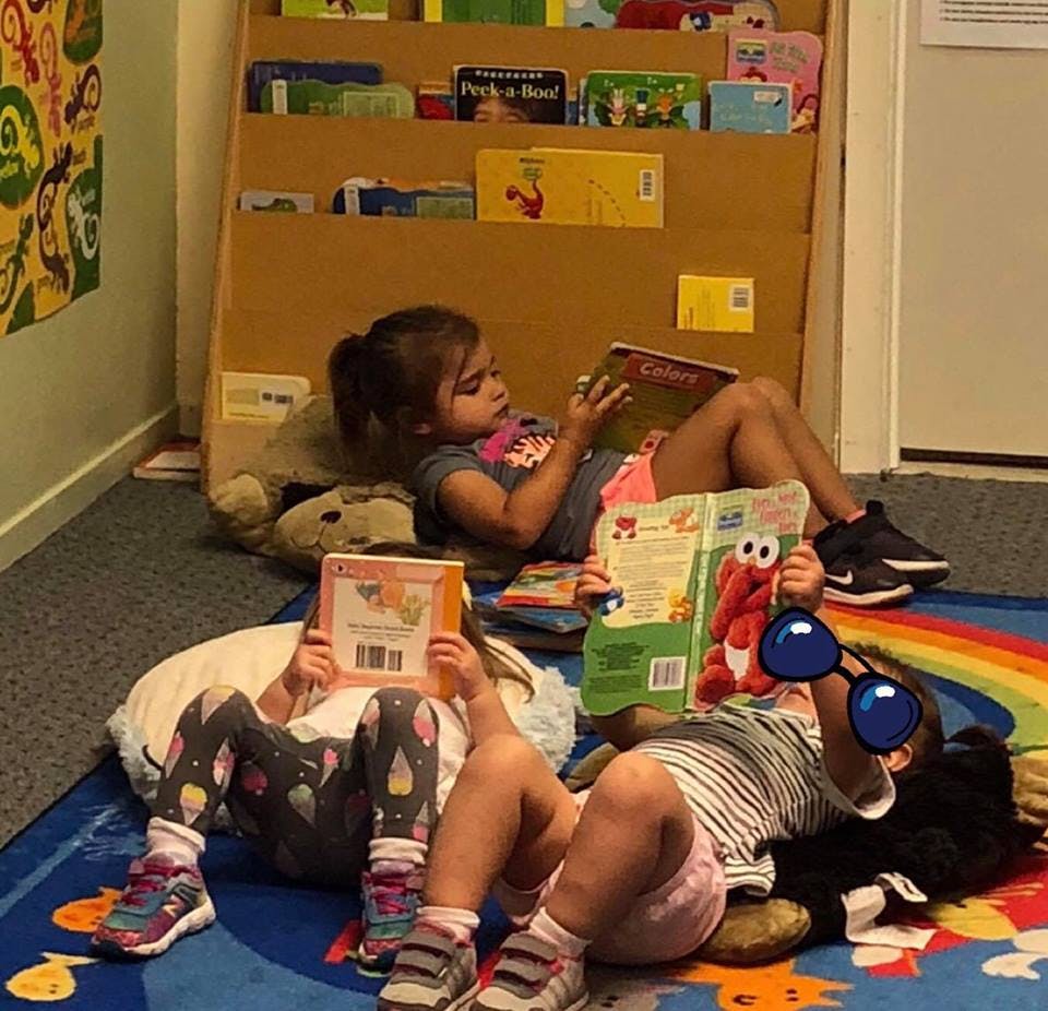 Three children lying on a rug reading books