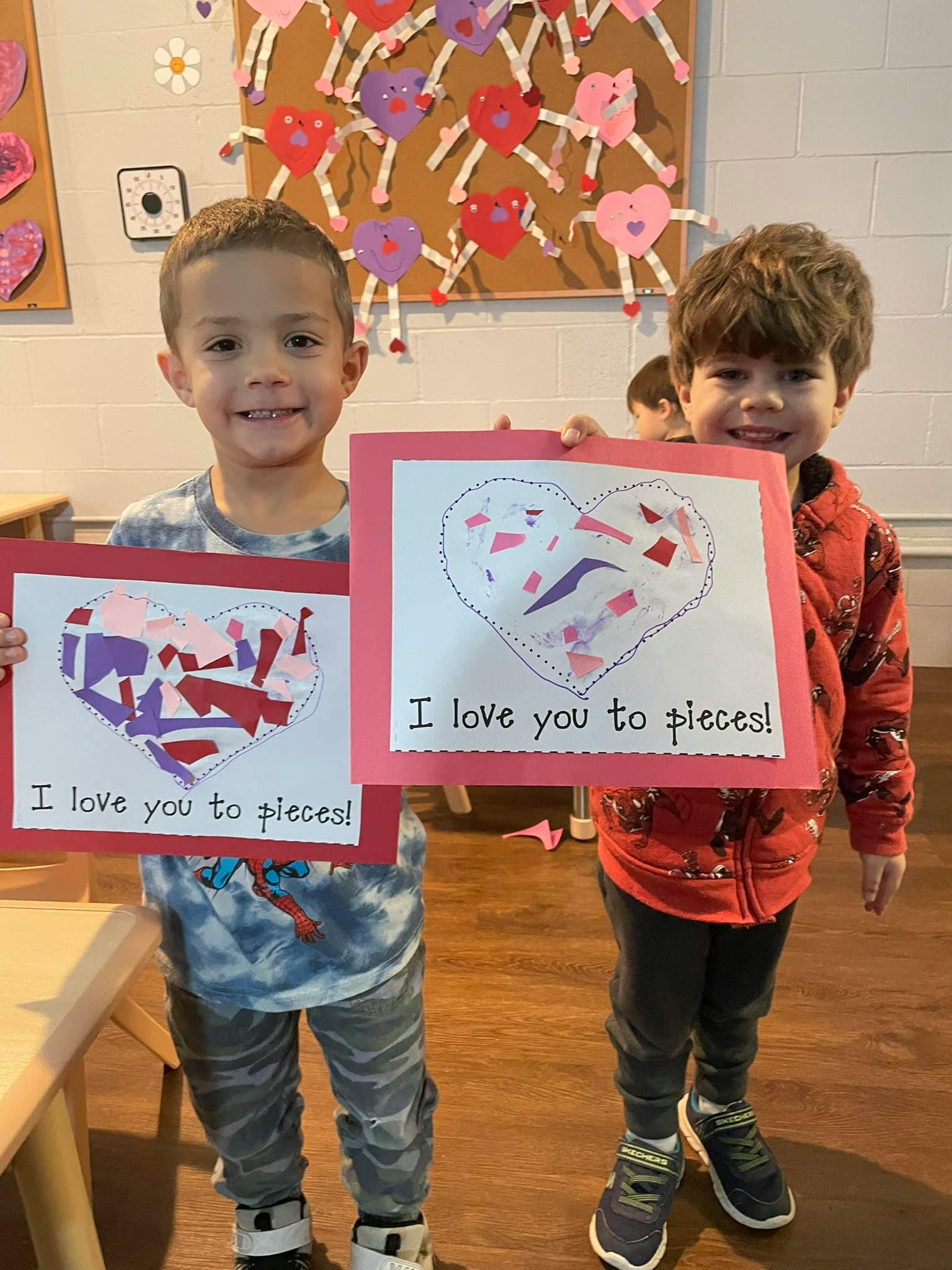 Two children holding up heart-shaped crafts that say "I love you to pieces!"