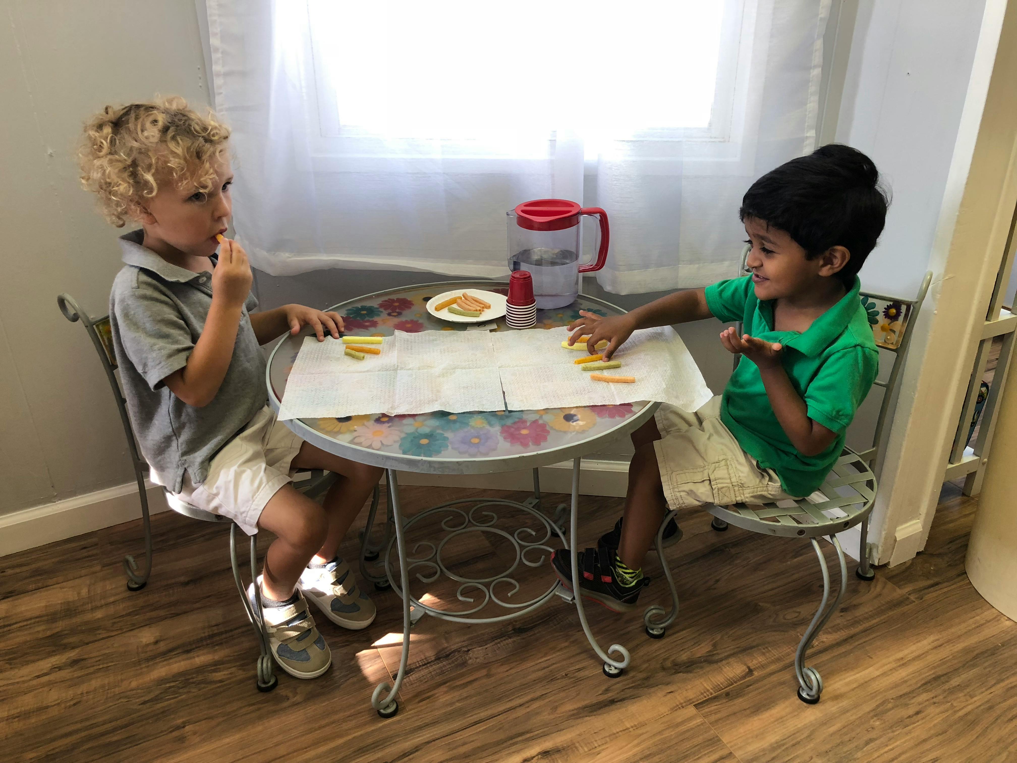 Two children sitting at a small table with snacks