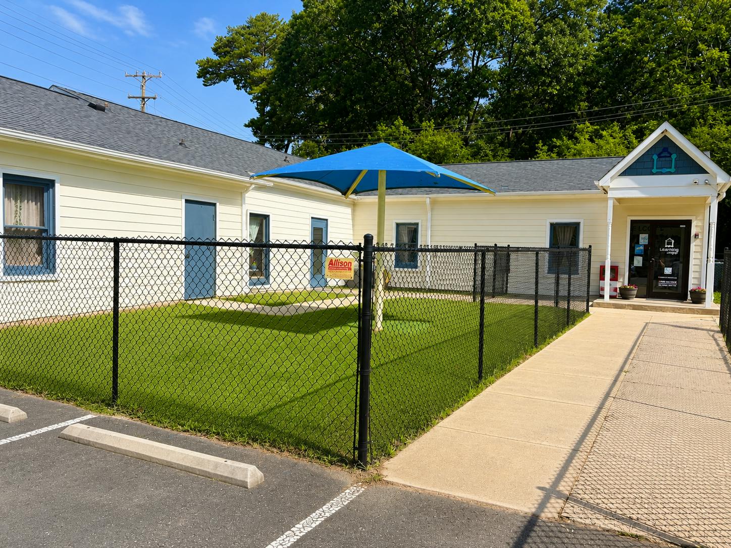 Fenced playground with blue shade structure next to a single-story building