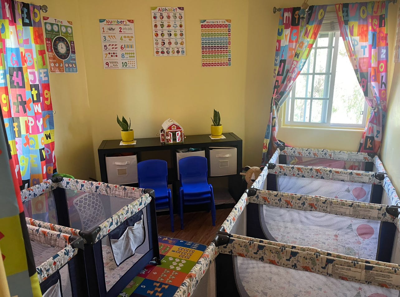 Three playpens in a room with colorful curtains and educational posters