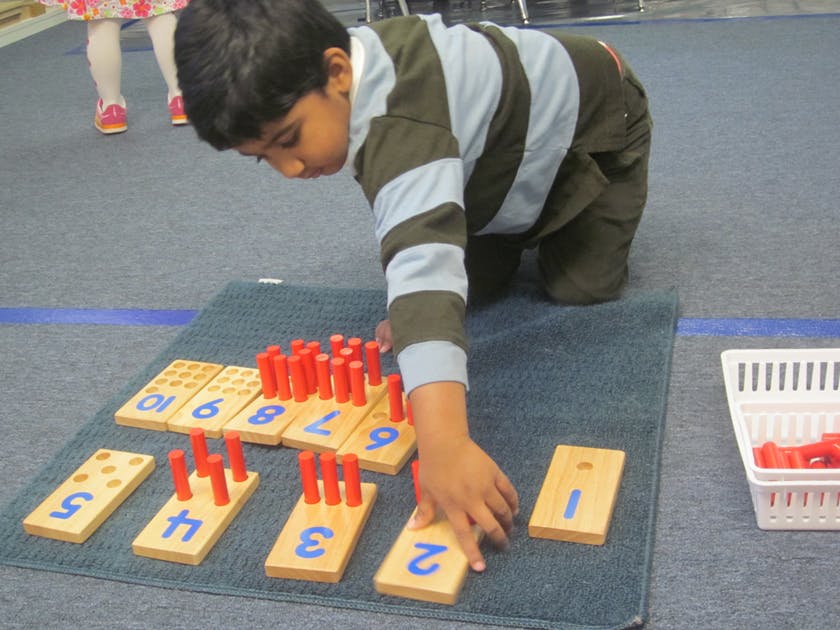 Child on knees playing with number blocks and red pegs