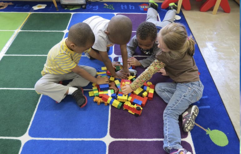 Four children playing with colorful building blocks on a patterned rug