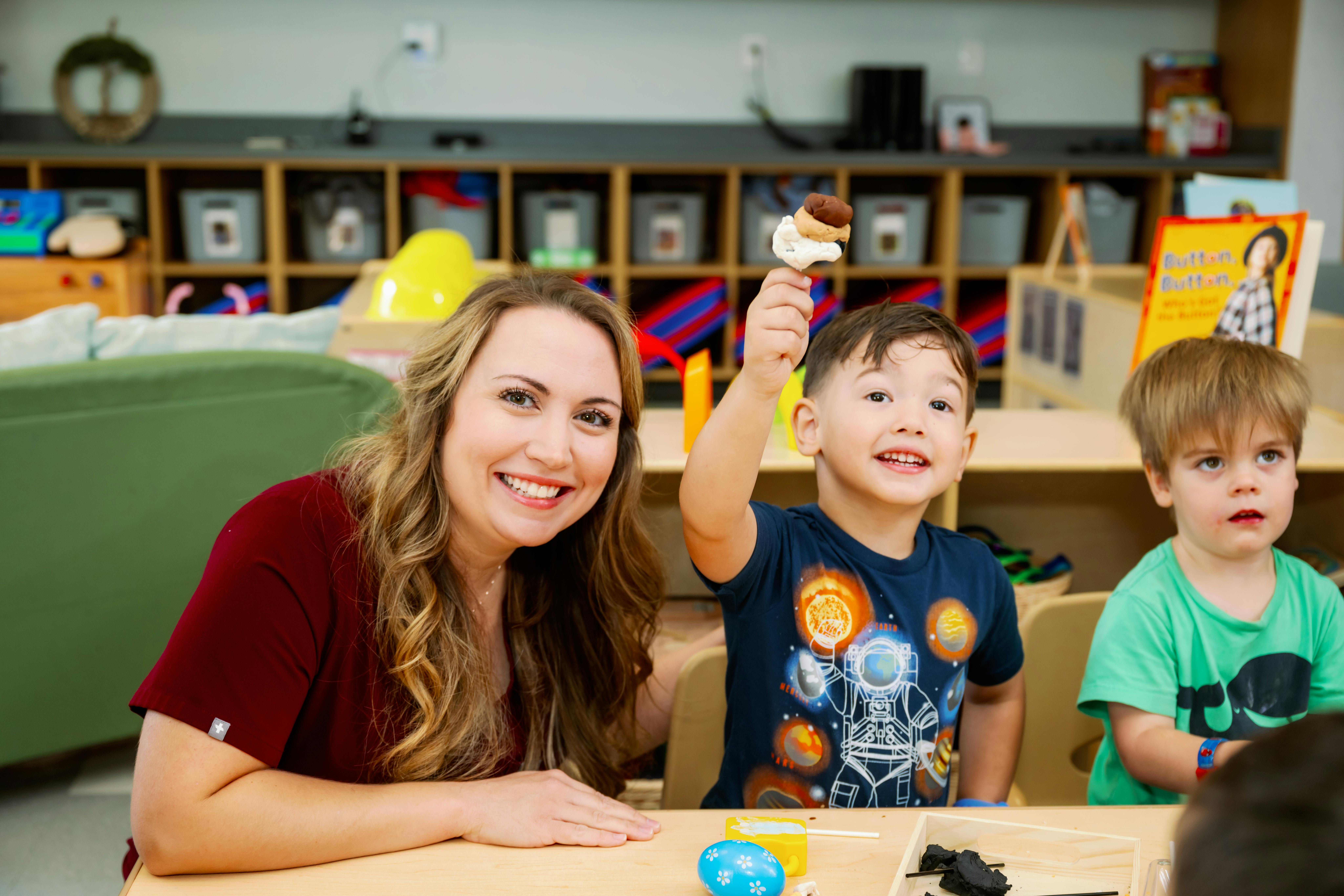 Person and two children at a table, one child holding up a toy