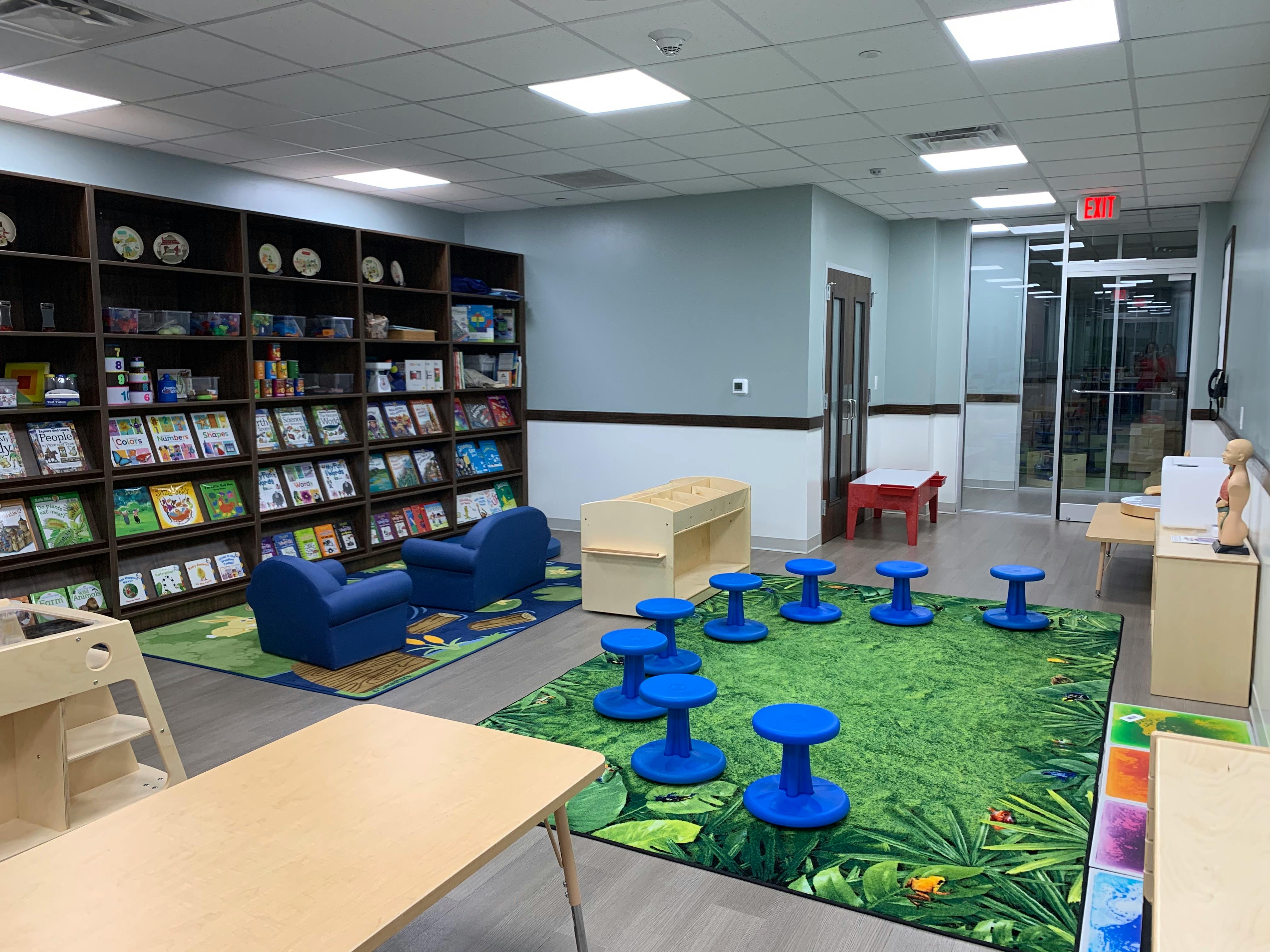 Children's reading area with bookshelves, blue chairs, and green rug with blue stools