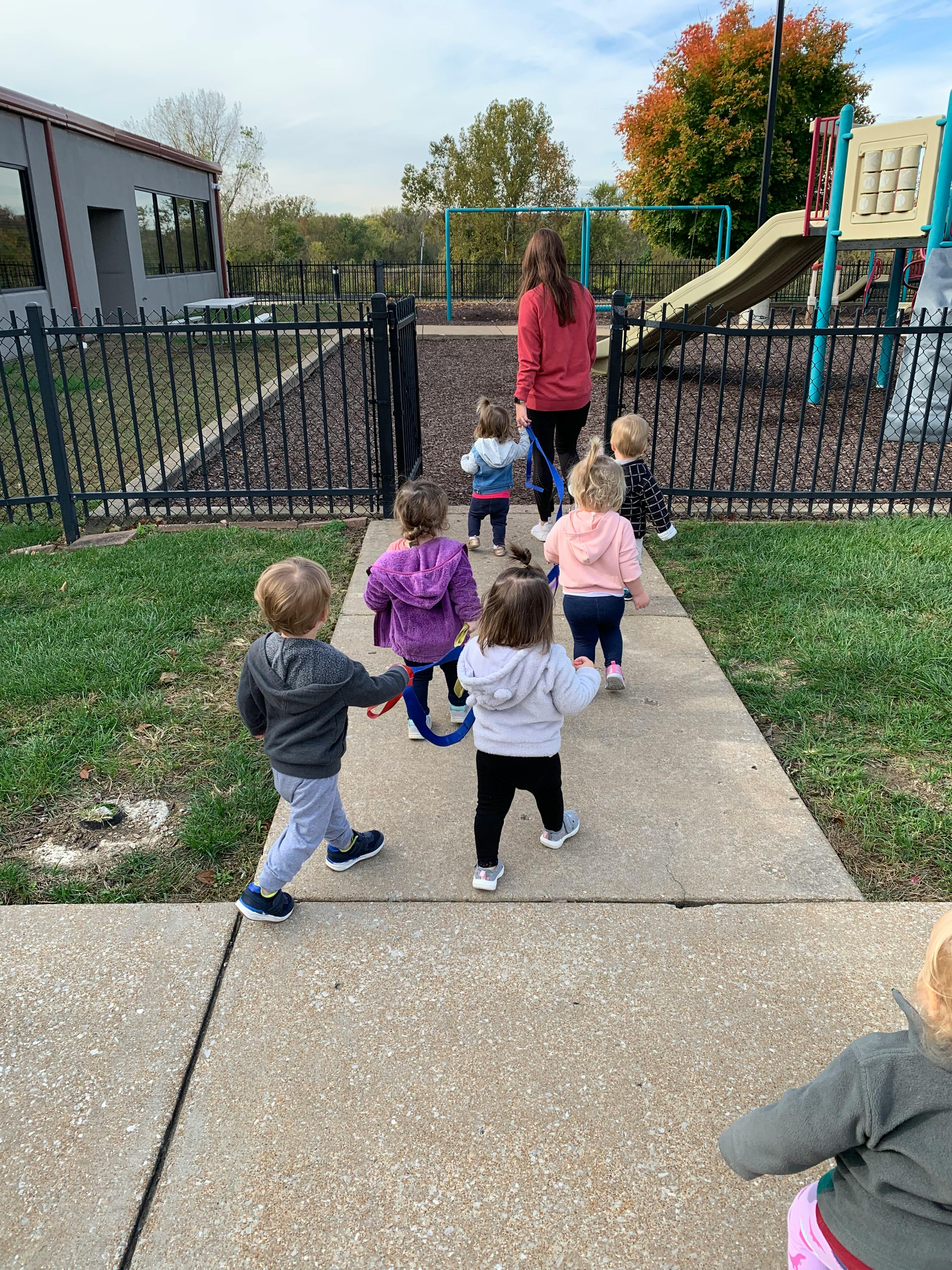 Group of children walking in a line holding a safety rope on a sidewalk