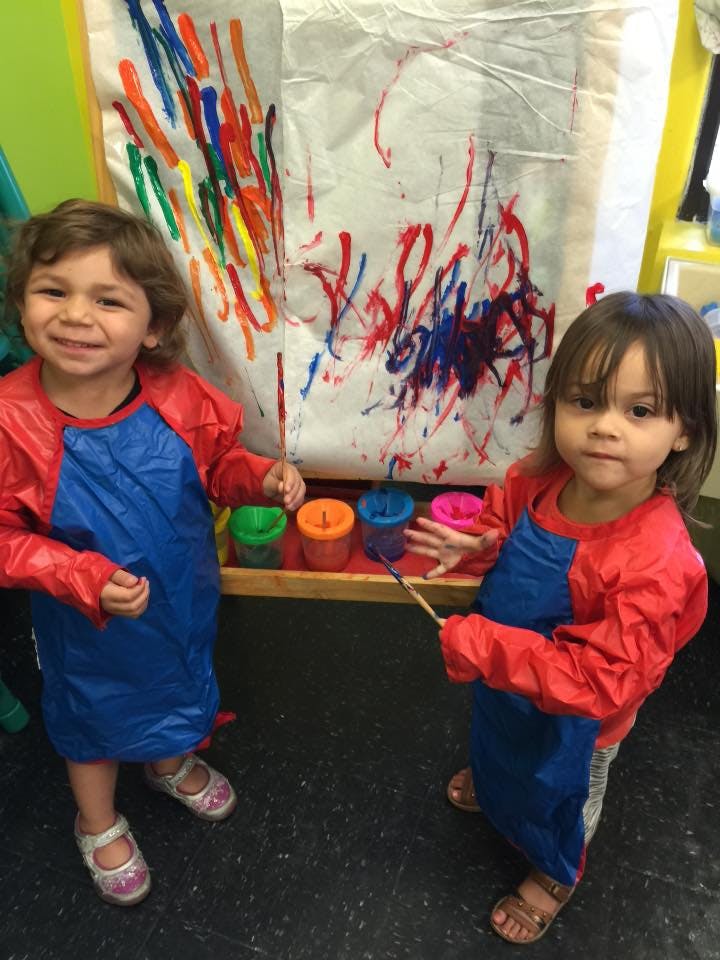 Two children in smocks painting on a large sheet of paper