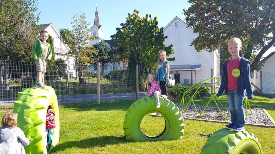 Children playing on green tires in a grassy area