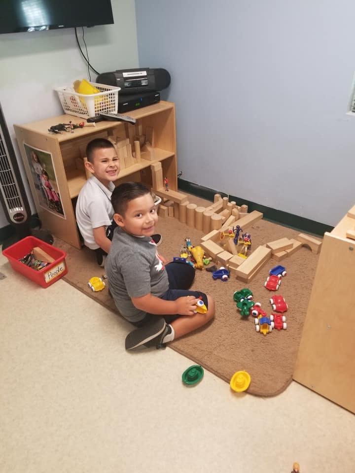 Two children playing with wooden blocks and toy cars on a rug