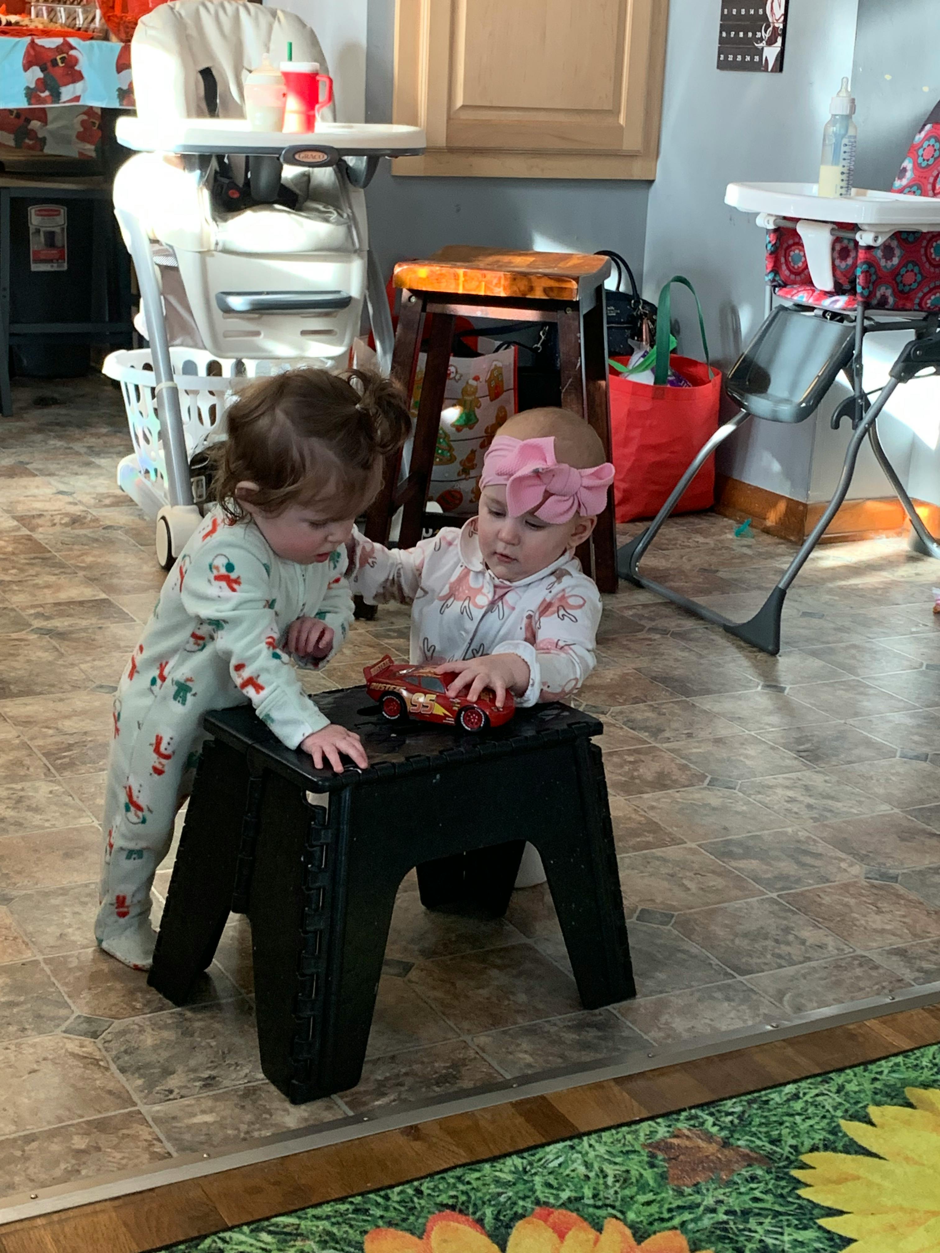 Two children playing with a toy car on a small stool
