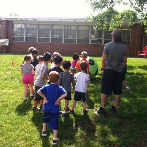 Adult and children gathered around a large green ball on a grassy field