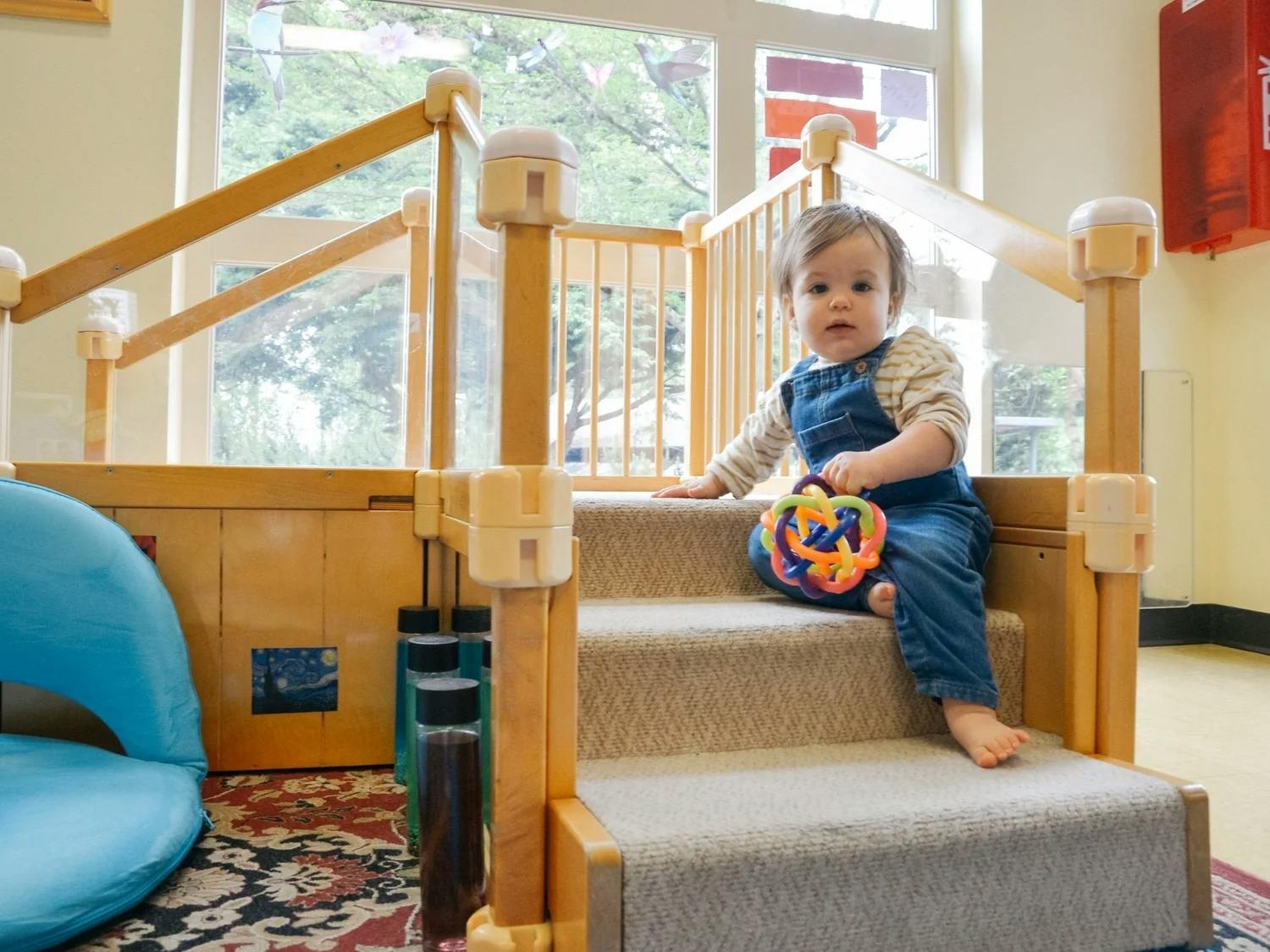 Child sitting on carpeted stairs with a colorful toy