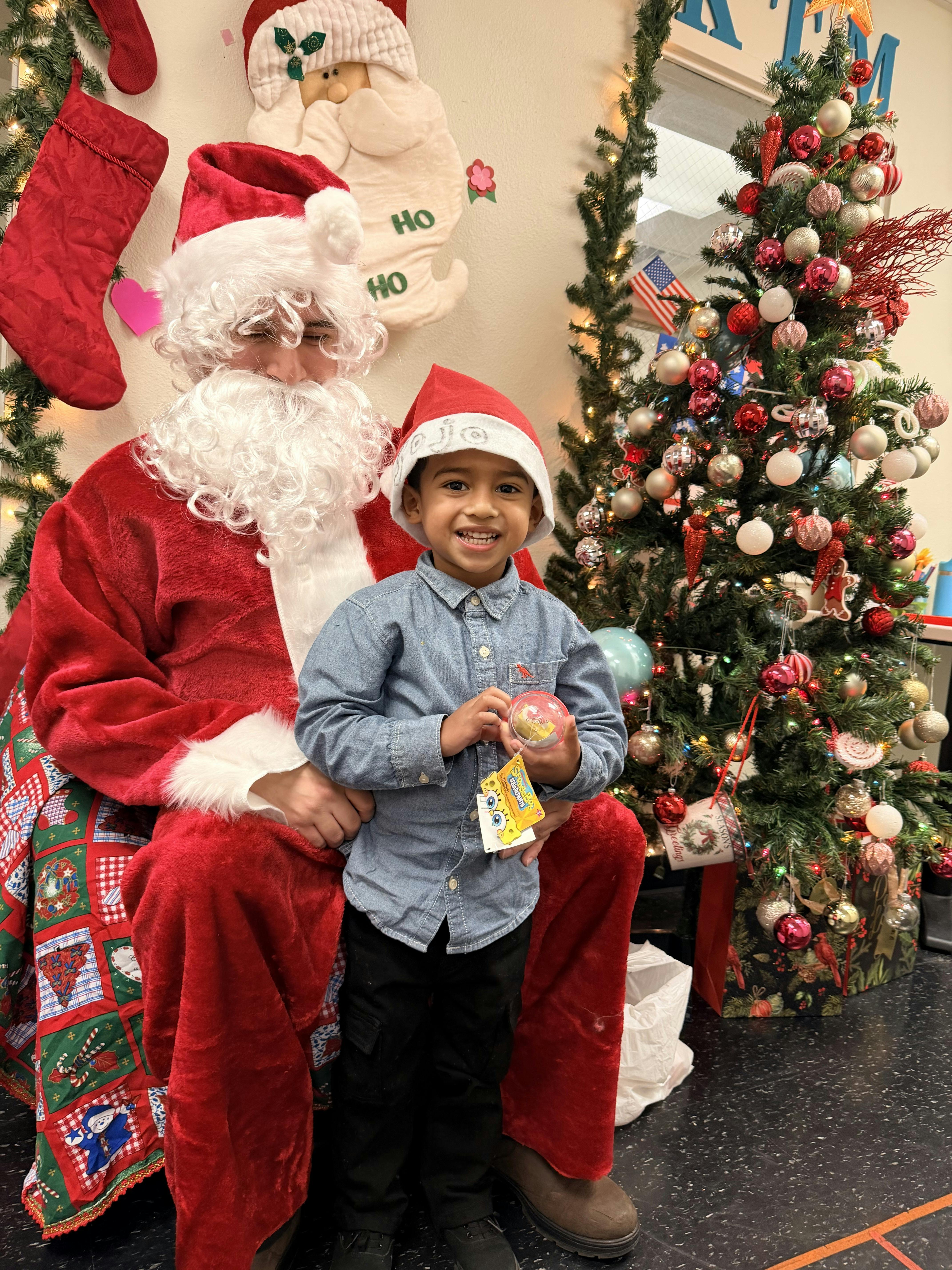Santa Claus sitting with a child wearing a Santa hat and holding a toy