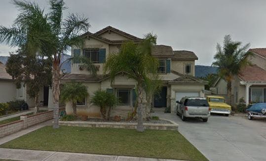 Two-story house with palm trees and cars in the driveway