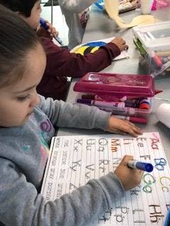 Child writing letters on a worksheet with a marker