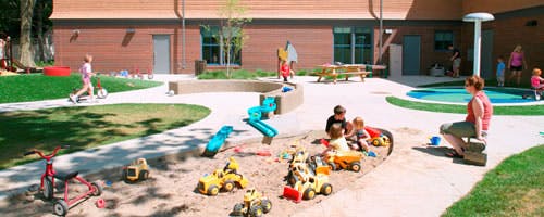 Children playing in a sandbox with toys and a person watching