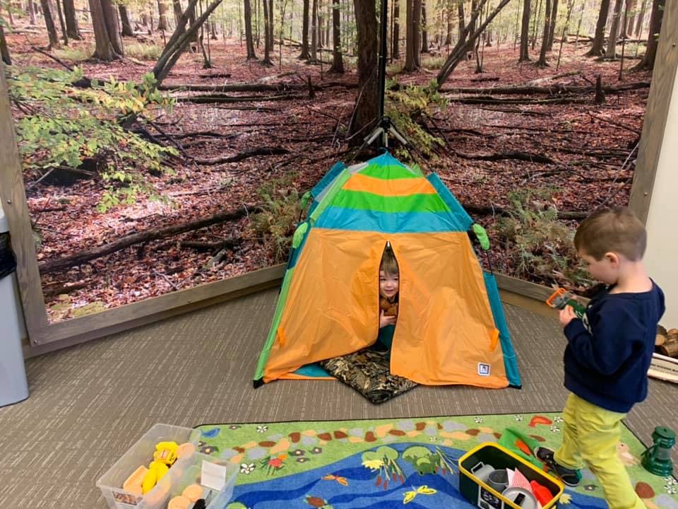 Child in a play tent and another child standing nearby