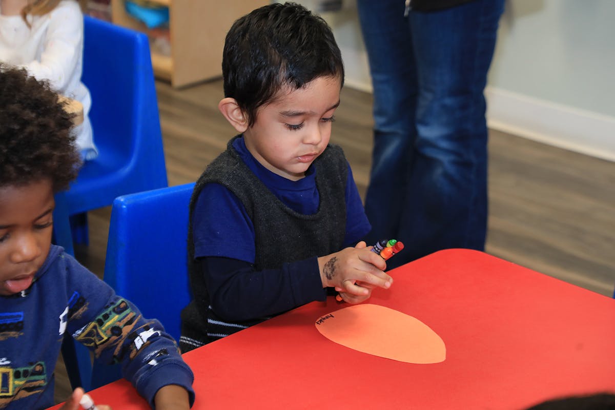 Child at a red table holding a small object, with another child nearby