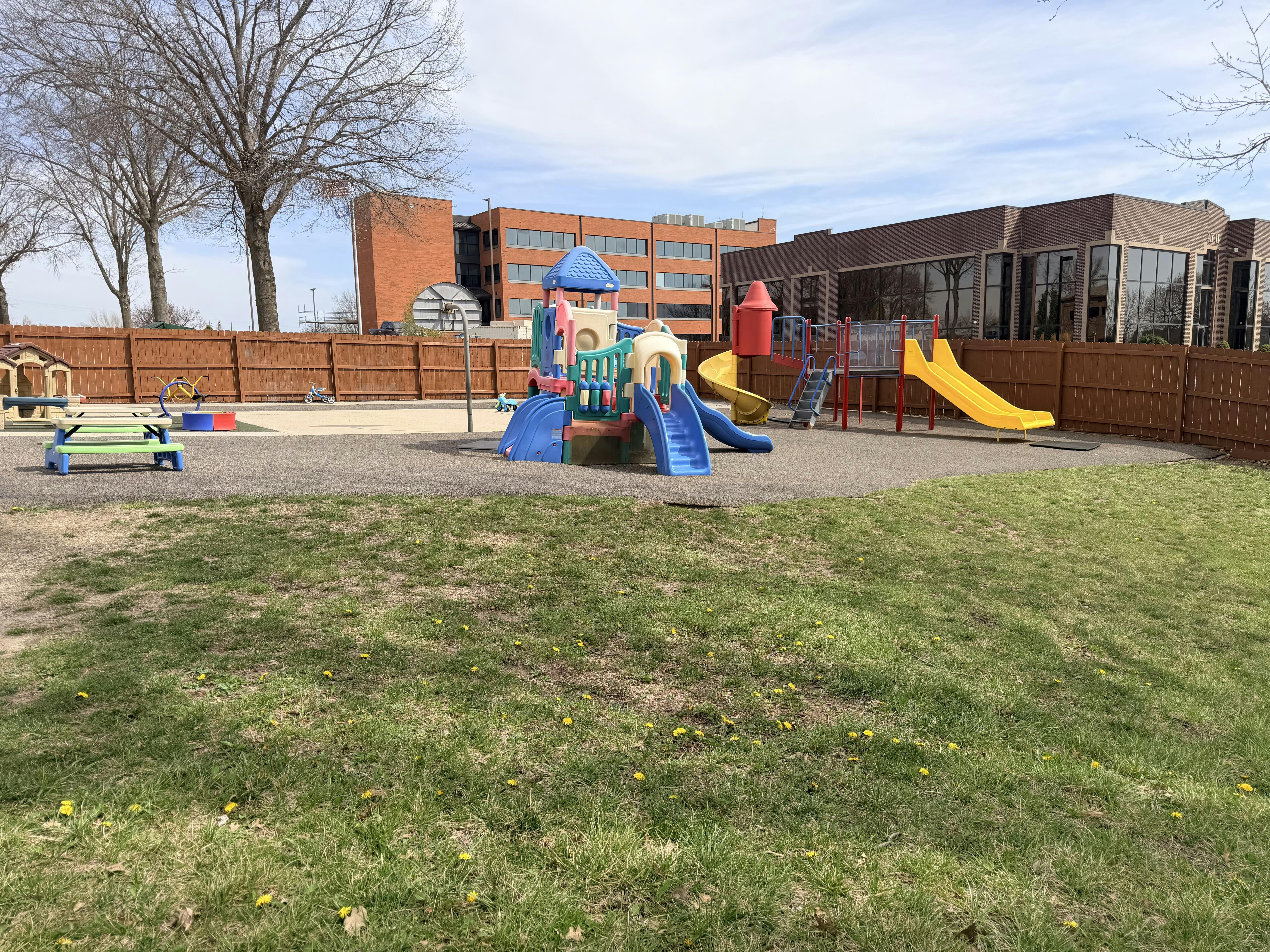 Playground with slides and structures, surrounded by a fence and building