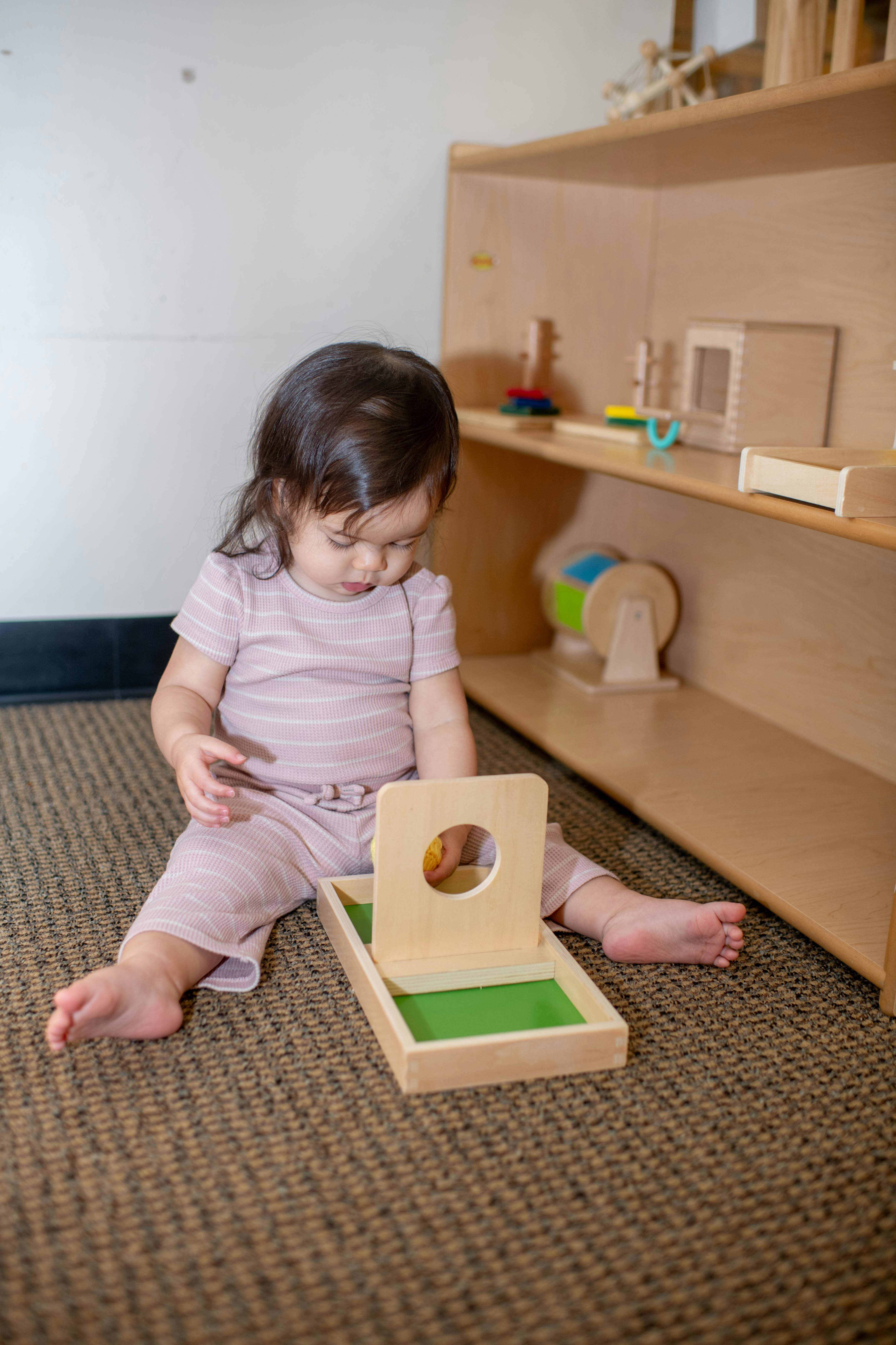 Child playing with a wooden ball and box toy on a carpeted floor