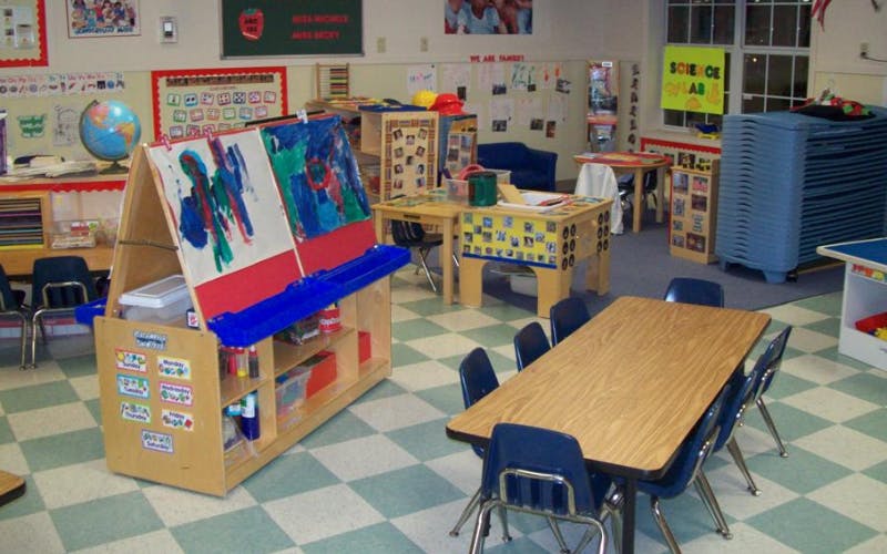 An empty classroom with an easel, tables, chairs, and learning materials