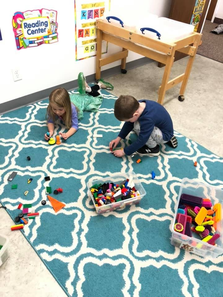Two children playing with building blocks on a rug in a classroom