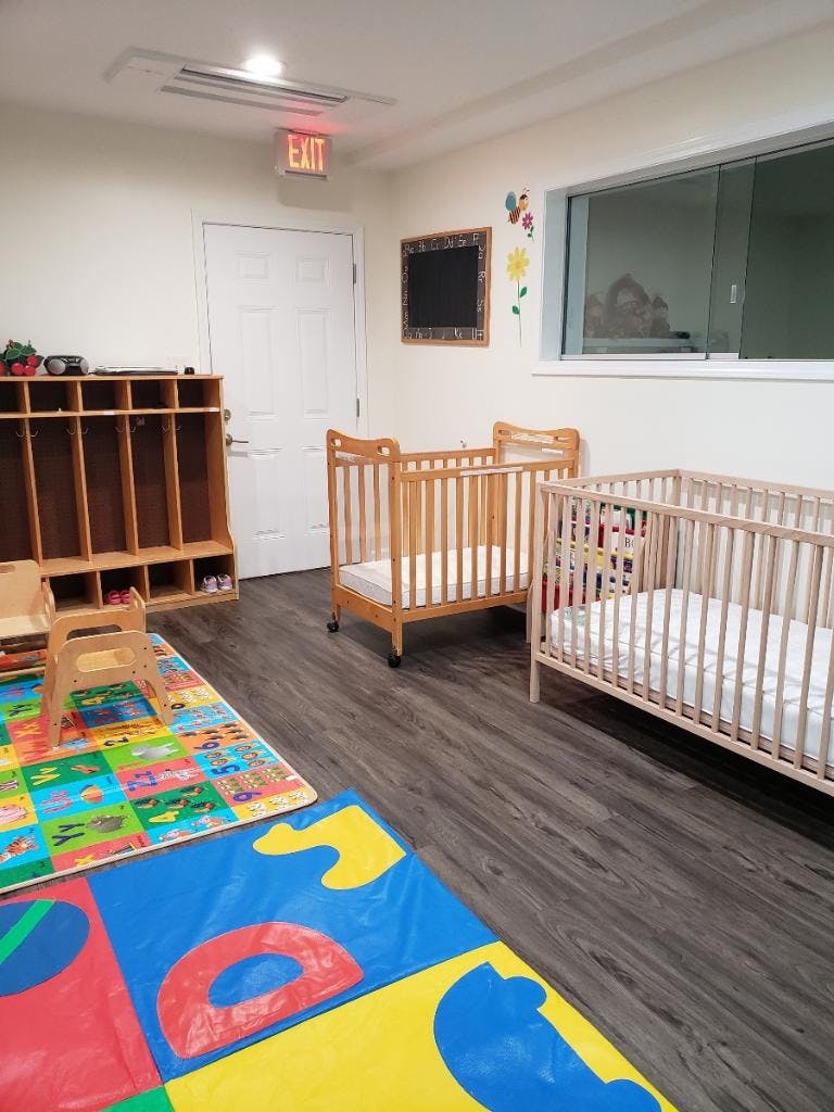 Two cribs in a room with colorful playmats and cubbies
