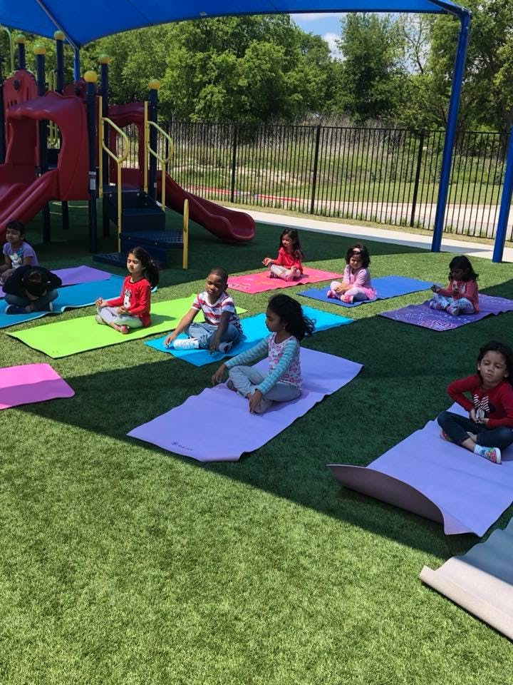 Children sitting on yoga mats on artificial grass