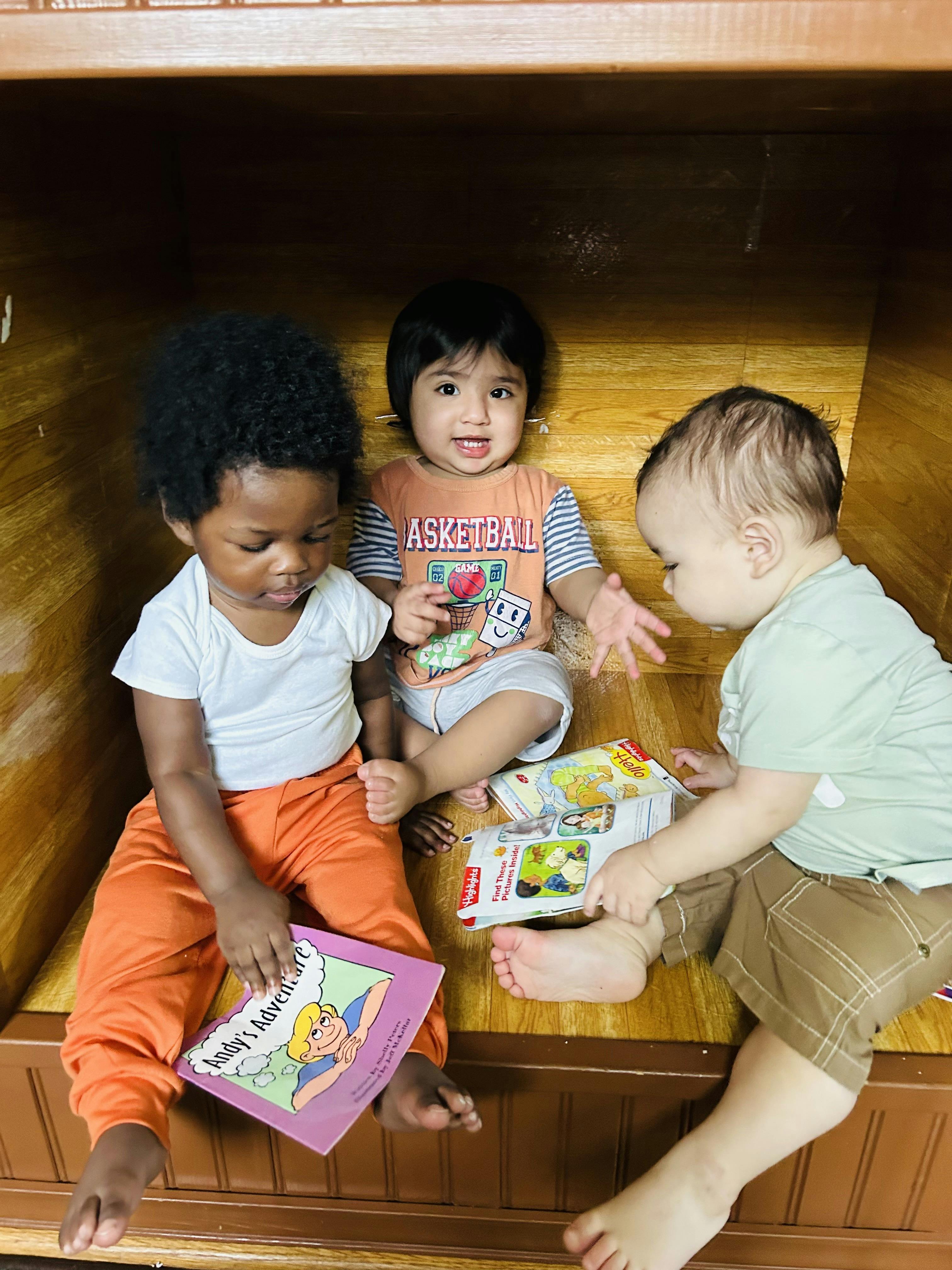 Three children sitting together on a wooden surface, holding books