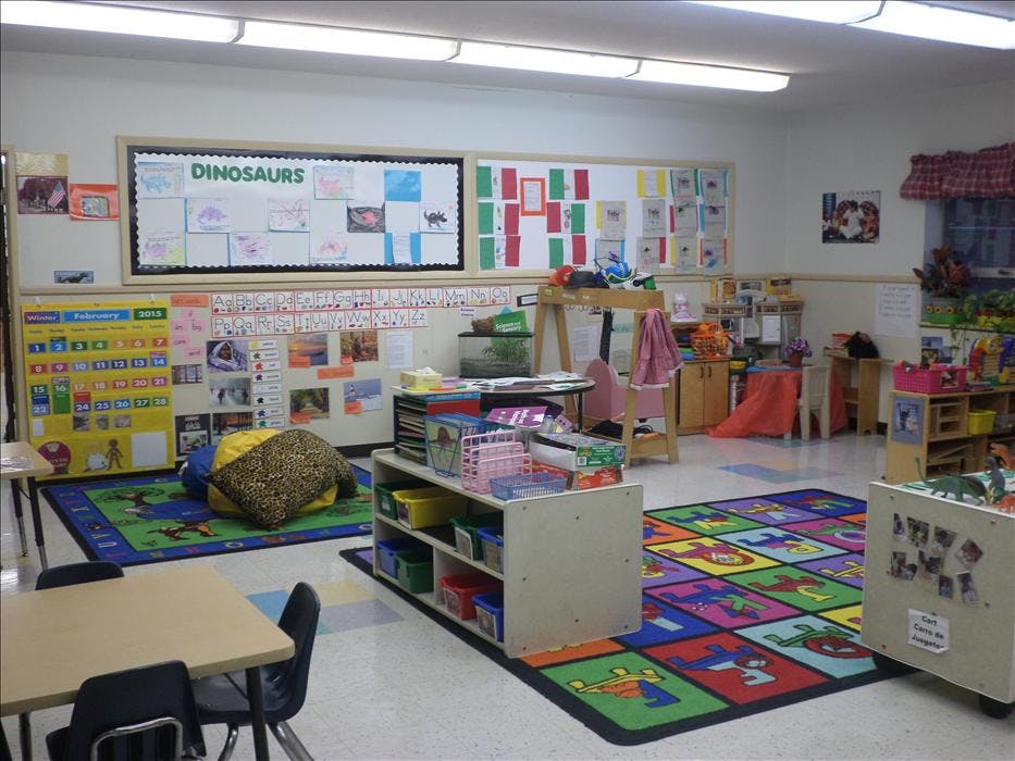 Classroom with colorful rugs, a calendar, shelves, and a bulletin board that says "Dinosaurs"