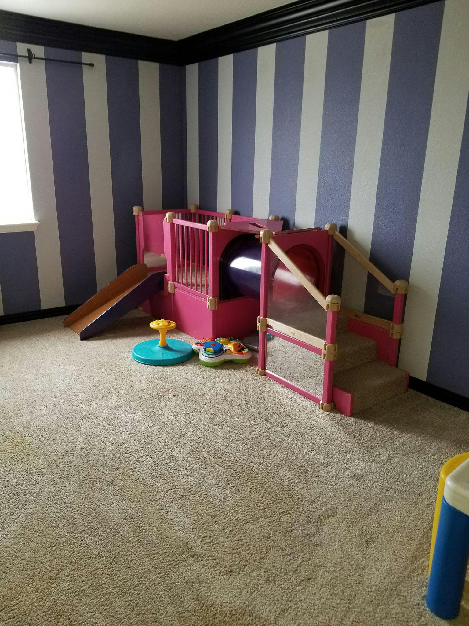 Indoor play structure with slide and tunnel in a room with striped walls