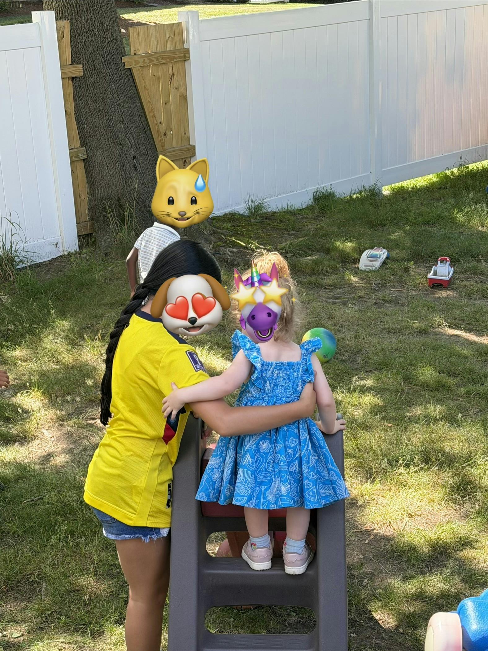 A person standing by a child on a small plastic slide in a backyard