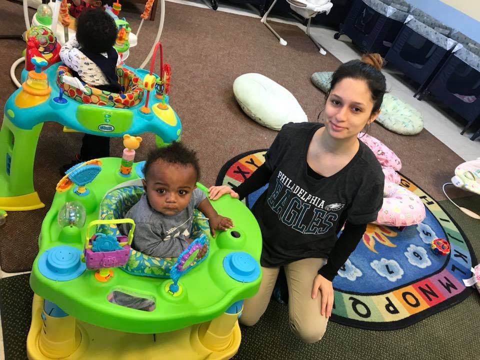 Person kneeling next to a child in a baby activity center